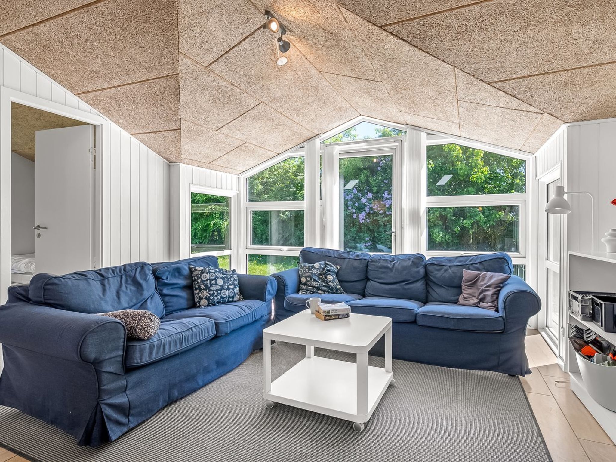 Ein Wintergarten mit zwei blauen Sofas, einem weißen Couchtisch und großen Fenstern mit Blick auf Grünflächen.