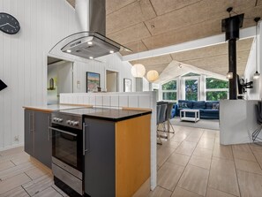 Eine moderne Küche mit Kochinsel, ein Essbereich mit einer Couch und ein großes Fenster mit Blick ins Freie.