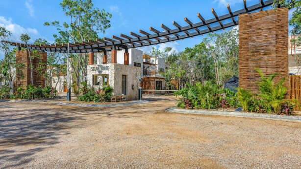 A gravel driveway leading to a building with a stone facade, a wooden pergola, and surrounding greenery. - Boho Apartment with Pool & Cenotes  (Tulum)