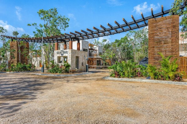 A gravel driveway leading to a building with a stone facade, a wooden pergola, and surrounding greenery. - Boho Apartment with Pool & Cenotes  (Tulum)