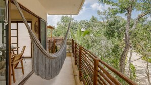 A balcony with a hammock, wooden furniture, and a view of trees. - Boho Apartment with Pool & Cenotes  (Tulum)