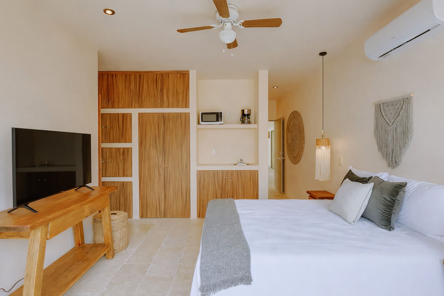 A bedroom with a TV, wooden wardrobe, bed, bedside table, and ceiling fan.