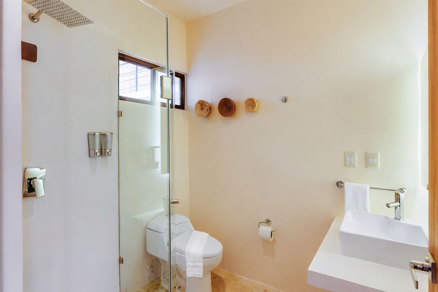 Un baño con cabina de ducha de vidrio, inodoro blanco, lavamanos y perchero para toallas.