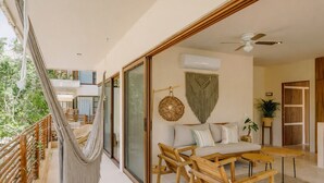 A balcony with a hammock, a sofa set, and a dining table. - Boho Apartment with Pool & Cenotes  (Tulum)