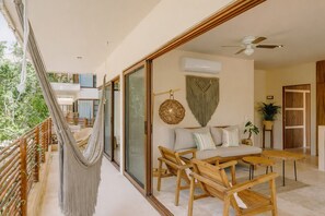 A balcony with a hammock, a sofa set, and a dining table. - Boho Apartment with Pool & Cenotes  (Tulum)
