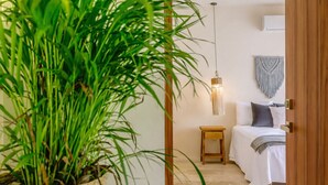 A room with a bed, bedside table, hanging light fixture, macrame wall hanging, and a potted plant. - Boho Apartment with Pool & Cenotes  (Tulum)