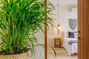A room with a bed, bedside table, hanging light fixture, macrame wall hanging, and a potted plant. - Boho Apartment with Pool & Cenotes  (Tulum)