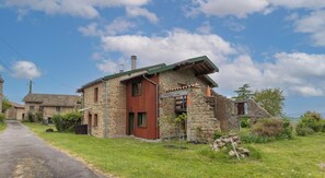 A stone house with a red door, a stone chimney, and a small garden. - Gîte chez Luc - SAINT FLOUR L'ETANG (SAINT FLOUR L'ETANG)
