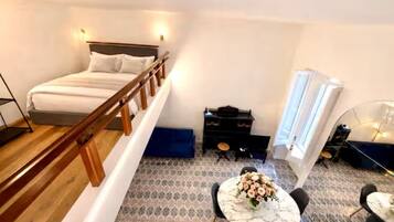 A bedroom with a bed, wooden railing, a small table with flowers, a piano, and a window.