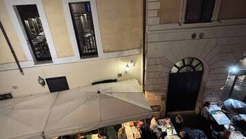 An outdoor dining area with tables and chairs, a white umbrella, and a building with a stone facade and windows.