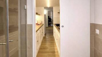 A modern kitchen with a wooden floor, white cabinets, and a glass shower enclosure.