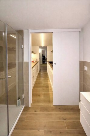 A modern kitchen with a wooden floor, white cabinets, and a glass shower enclosure. - Shelter in Navona Designer loft in Piazza Navona (Roma)