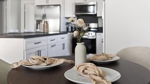 A modern kitchen with white cabinets, a stainless steel refrigerator, and a vase with flowers on a table.