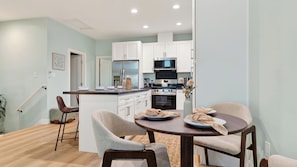 A modern kitchen with white cabinets, a central island, and a dining area with two chairs and a table.