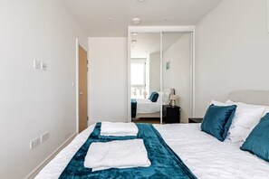 A hotel room with a bed, a mirror, a wardrobe, and a window. - Deluxe 2BR Flat with Gym, Cinema, Work Area, Free Parking, Games Room and Lounge (London)