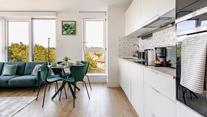 Eine moderne Küche mit weißen Schränken, ein Essbereich mit einem grünen Sofa und Stühlen sowie große Fenster mit Blick auf Bäume.