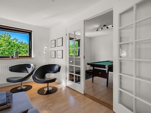 A modern room with a pool table, two black chairs, a window with a view of greenery, and framed pictures on the wall. - "Isalie" - 300m from the sea by Interhome (Ebeltoft)