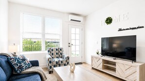Una sala moderna con sofá, sillón, mesa de centro, televisor y aire acondicionado instalado en la pared.