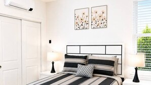 Un dormitorio con cama, mesitas de noche, persianas en la ventana y decoración en la pared.