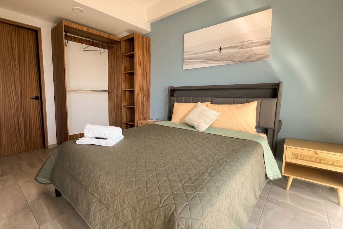 Une chambre Ă coucher comprenant un lit, une armoire en bois, une table de chevet et une Ćuvre dâart accrochĂ©e au mur.