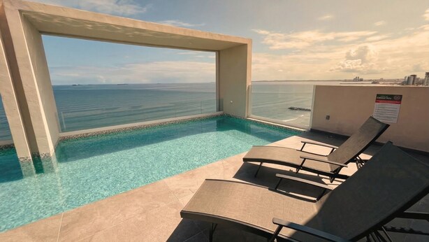 Ein Pool mit klarem Wasser, Meerblick und Liegestühle auf einem Balkon.