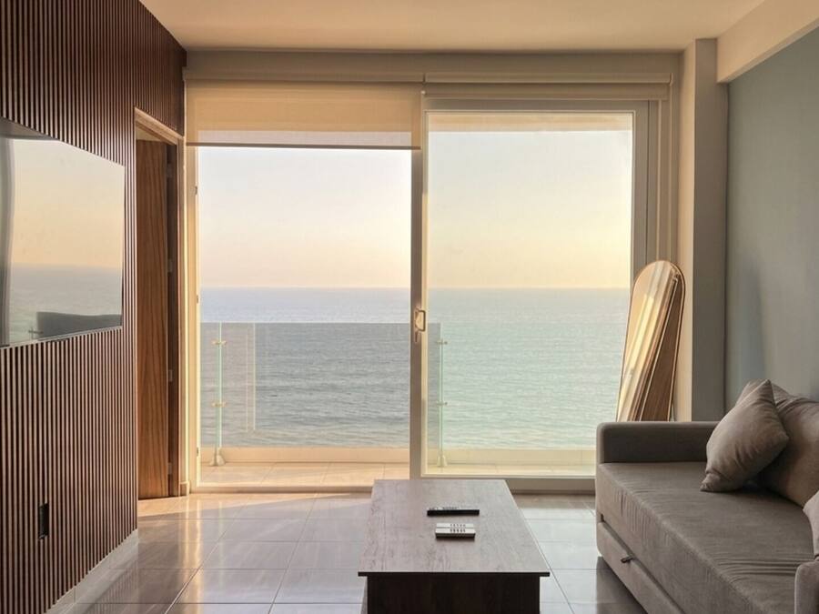 Una sala de estar moderna con un amplio ventanal corredera que da a un balcón con vista al mar.