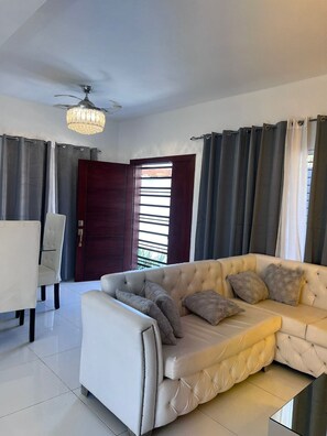 A living room with a sofa, a chair, a ceiling fan, and a view through a door.