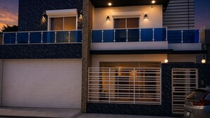 A modern two-story building with a garage, a balcony, and a car parked in front.
