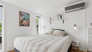 Ein Schlafzimmer mit einem Bett, Nachttischen, einer Wand-Klimaanlage und einem Fenster.