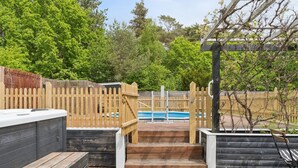 Eine Holzterrasse führt zu einem Poolbereich mit Zaun und Whirlpool.