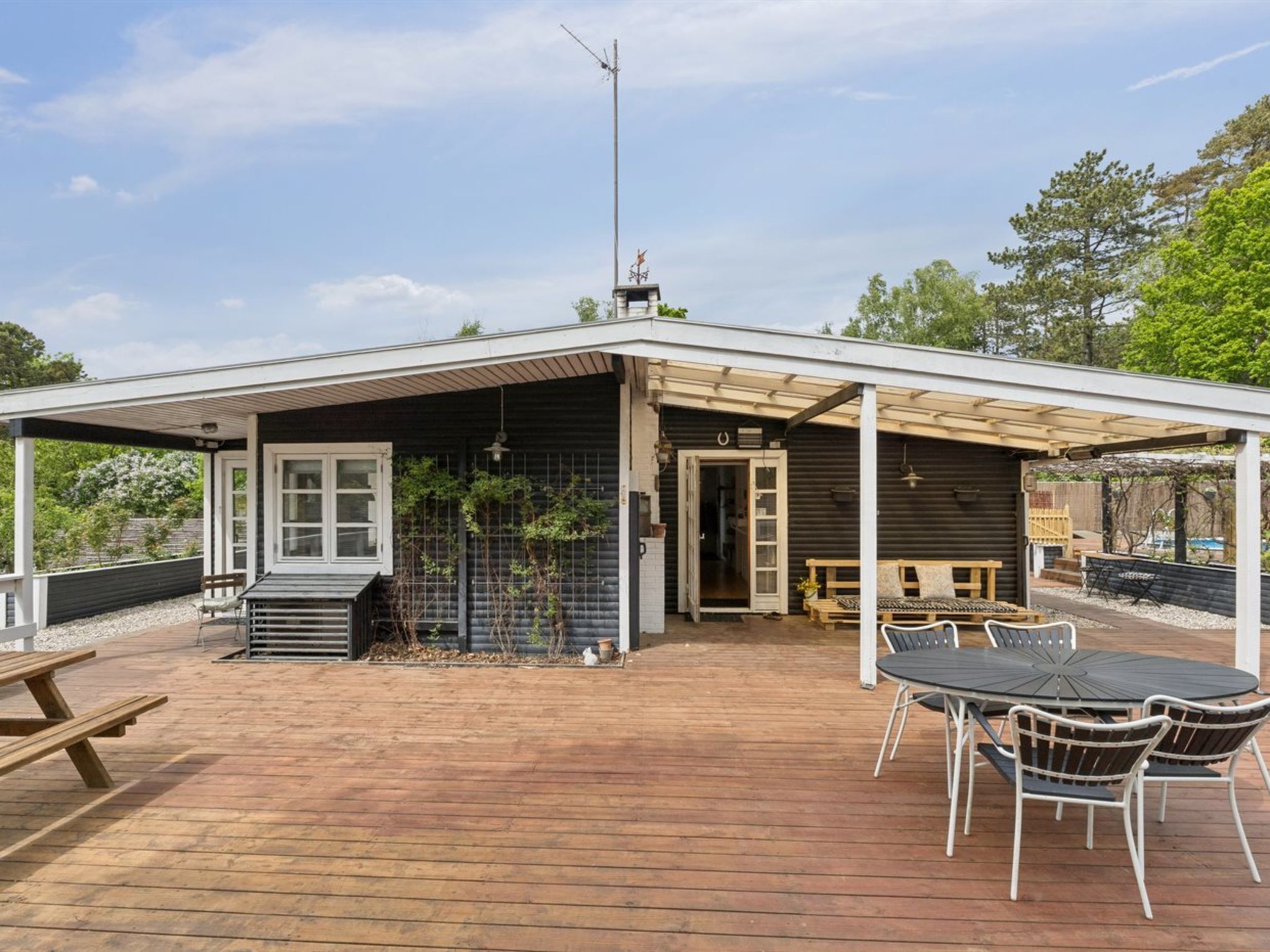 Eine Holzterrasse mit überdachter Veranda, einem Tisch mit Stühlen und einer Bank.