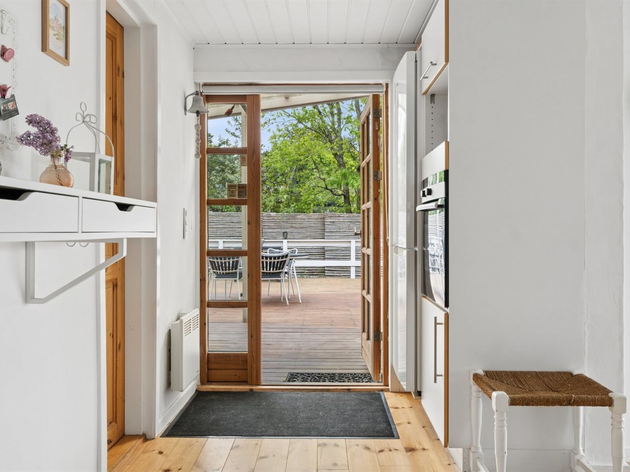 A narrow hallway with a wooden door leading to an outdoor deck, a white radiator, and a small shelf with decorative items.