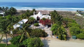 Une propriété située en bord de mer, avec un bâtiment blanc, des palmiers et une vue sur l’océan.