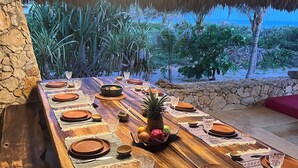 Une longue table à manger en bois, dressée avec des assiettes, des verres et un centre de table composé de fruits et d’un ananas.