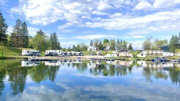 A lakeside RV park with multiple RVs and trailers, calm water reflecting the sky, and surrounding greenery.