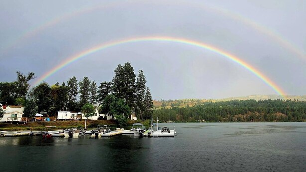 Ein See mit Regenbogen, Booten und Häusern am Ufer.