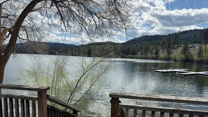 Blick auf einen See mit einem Holzsteg und einem Haus im Hintergrund.