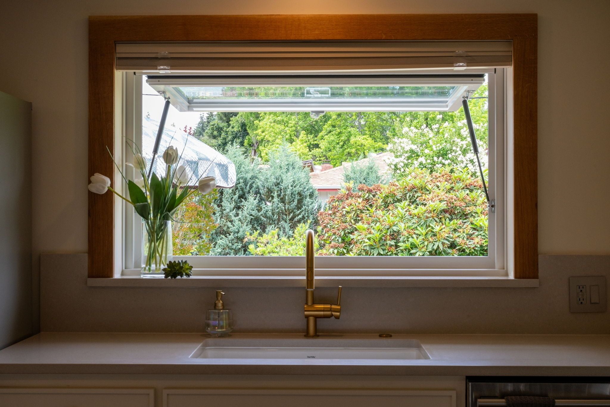 A kitchen with a window, a sink, and a vase with flowers.