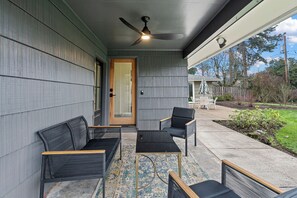 Eine überdachte Veranda mit Gartenmöbeln, einem Deckenventilator und Blick auf den Garten.
