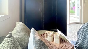 Une pièce comprenant une grande armoire, un canapé, un plateau avec des objets décoratifs et une vue sur l’extérieur, visible à travers une porte.