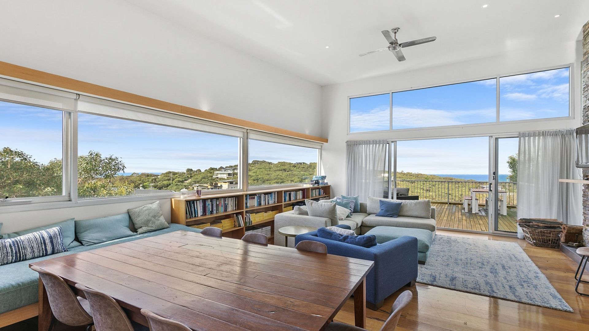 Un salón amplio con una gran mesa de madera, varias zonas de estar, una estantería y un balcón con vistas.