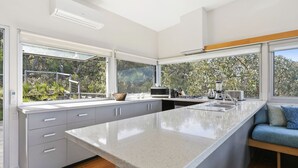 A modern kitchen with a large island, built-in appliances, and large windows offering a view of greenery. - Timbara Hideaway - Ocean Views - Pet Friendly (Fairhaven)