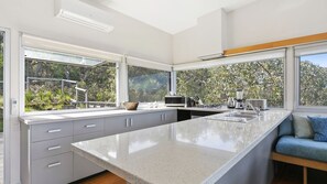 A modern kitchen with a large island, built-in appliances, and large windows offering a view of greenery. - Timbara Hideaway - Ocean Views - Pet Friendly (Fairhaven)