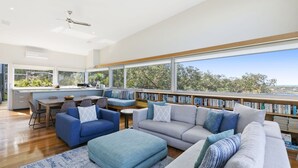 A modern living room with a large window, a built-in bookshelf, and a dining area. - Timbara Hideaway - Ocean Views - Pet Friendly (Fairhaven)