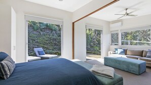 A bedroom with a large bed, a sofa, a chair, and a view of a garden through sliding glass doors. - Timbara Hideaway - Ocean Views - Pet Friendly (Fairhaven)