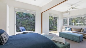 A bedroom with a large bed, a sofa, a chair, and a view of a garden through sliding glass doors. - Timbara Hideaway - Ocean Views - Pet Friendly (Fairhaven)