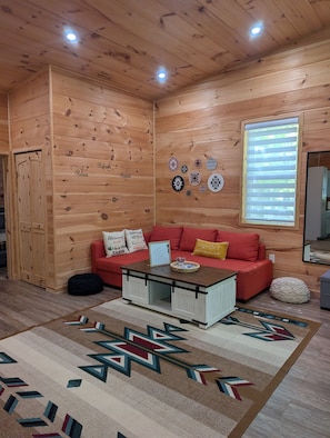 Ein gemütliches Blockhausschlafzimmer mit Holzbalkendecke, einem roten Sofa, einem Couchtisch und einem Teppich mit geometrischen Mustern.