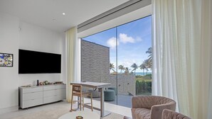 Una sala de estar moderna con televisor de pantalla plana, una mesa de comedor, un sofá y un gran ventanal corredero que da a un balcón con vistas a palmeras.