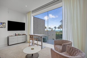 Ein modernes Wohnzimmer mit Flachbildfernseher, Esstisch, Sofa und einer großen Schiebeglastür, die auf einen Balkon mit Blick auf Palmen führt.