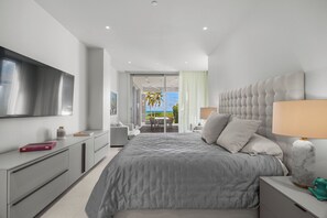 Ein modernes Schlafzimmer mit einem großen Bett, einem Fernseher, einem Schreibtisch und Blick ins Freie.